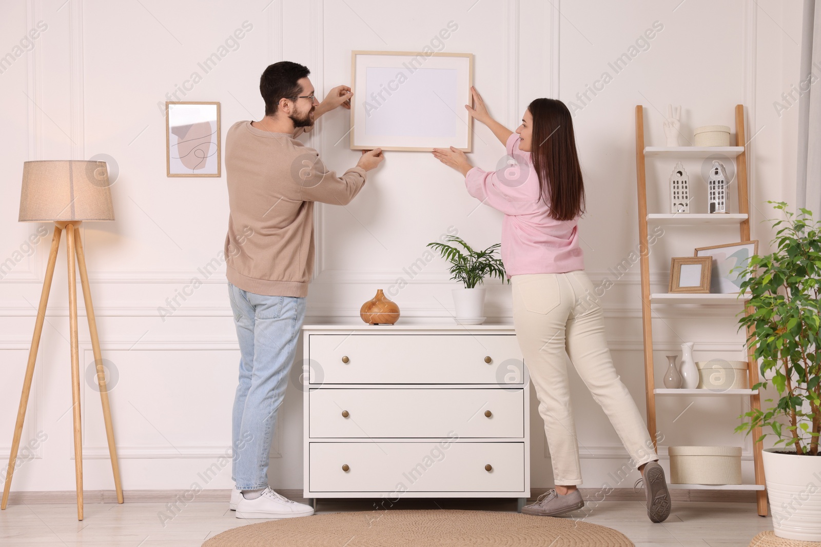 Photo of Man and woman hanging picture frame on white wall at home