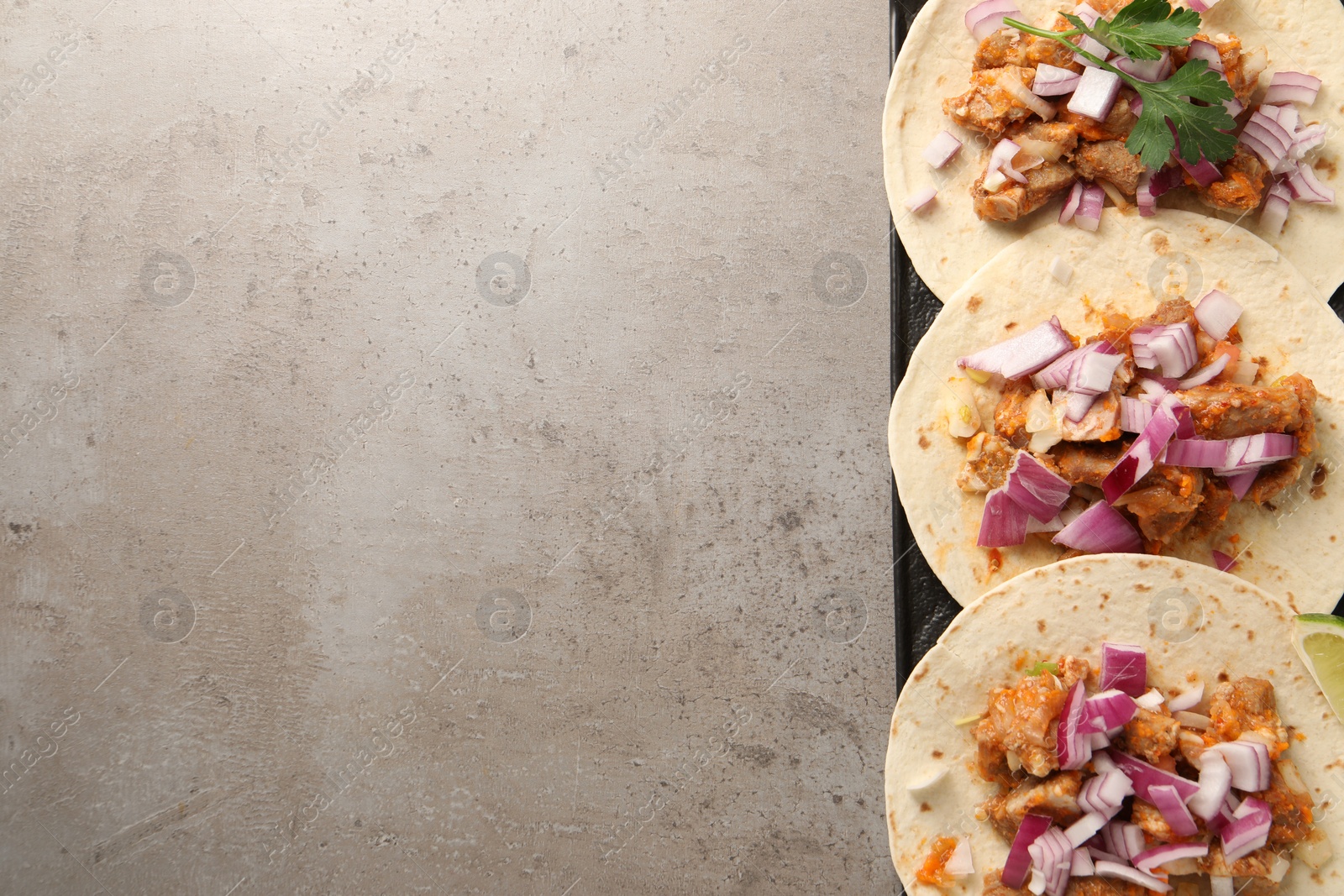 Photo of Delicious tacos with vegetables, meat and lime on grey textured table, top view. Space for text