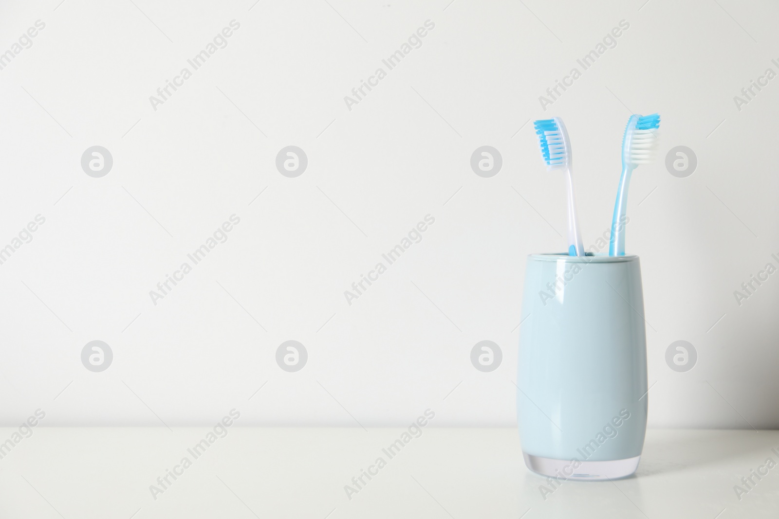 Photo of Plastic toothbrushes in holder on white table, space for text