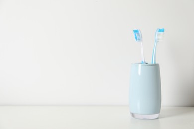 Photo of Plastic toothbrushes in holder on white table, space for text