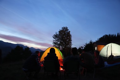 Group of friends near bonfire and camping tents outdoors in evening