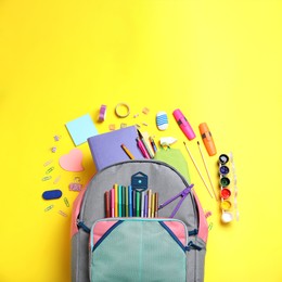 Image of Stylish backpack with different school stationery on yellow background, flat lay. Space for text