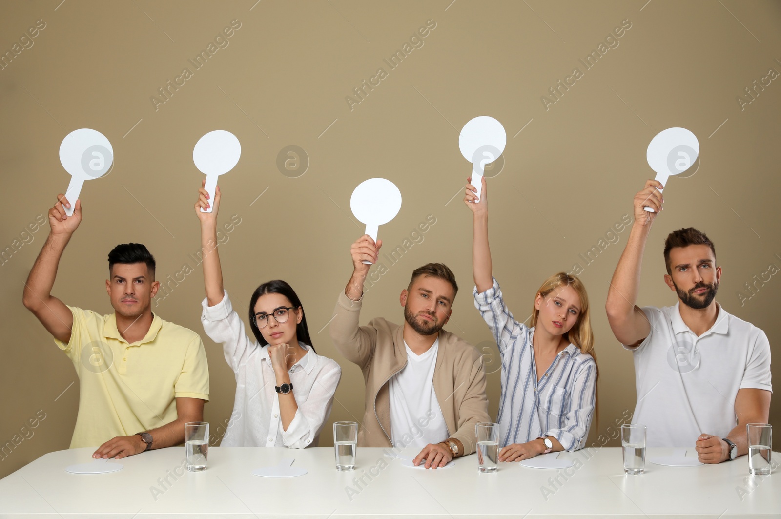 Photo of Panel of disappointed judges holding blank score signs at table on beige background. Space for text