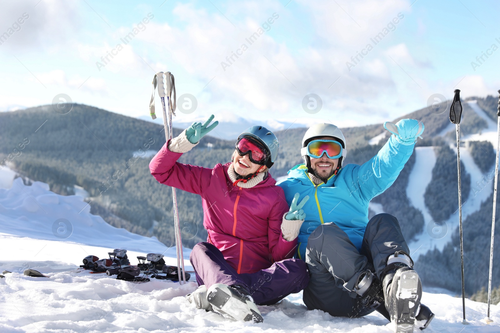 Photo of Happy couple with ski equipment sitting on snowy hill in mountains. Winter vacation