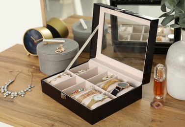 Photo of Elegant jewelry box with beautiful bijouterie and expensive wristwatches near luxury perfume on wooden table