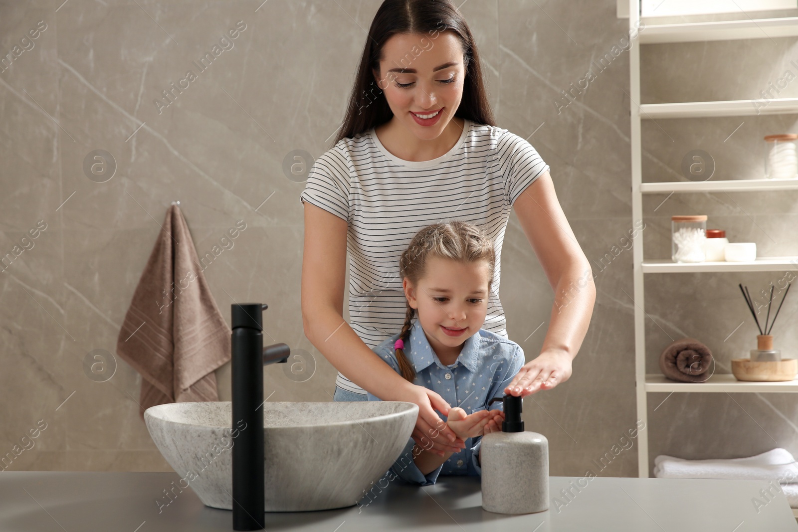 Photo of Mother and daughter washing hands with liquid soap together in bathroom