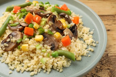 Delicious bulgur with vegetables and mushrooms on wooden table, closeup