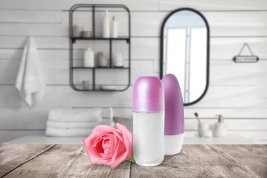 Image of Different roll-on deodorants and pink rose on wooden table in bathroom. Mockup for design