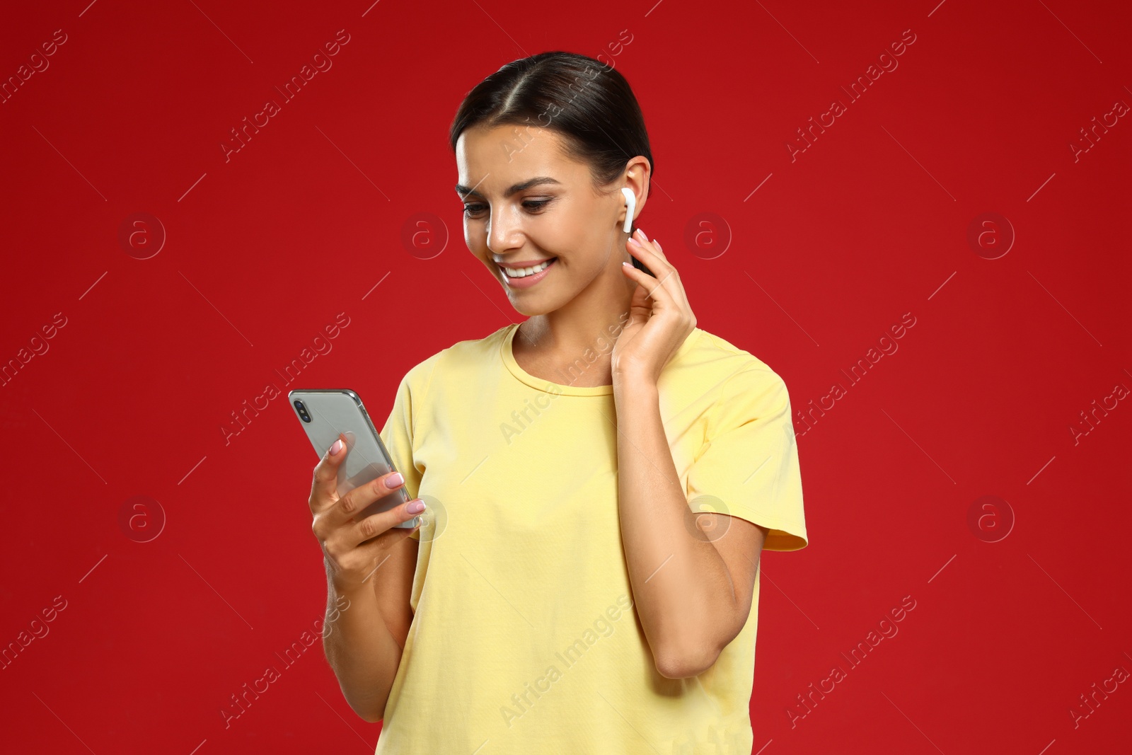 Photo of Happy young woman with smartphone listening to music through wireless earphones on red background