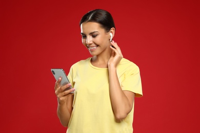 Photo of Happy young woman with smartphone listening to music through wireless earphones on red background