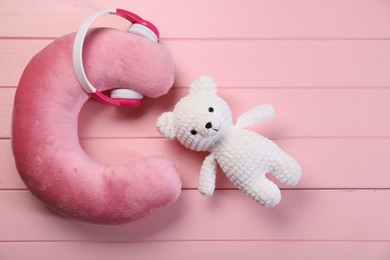 Photo of Travel pillow, toy bear and headphones on pink wooden background, flat lay