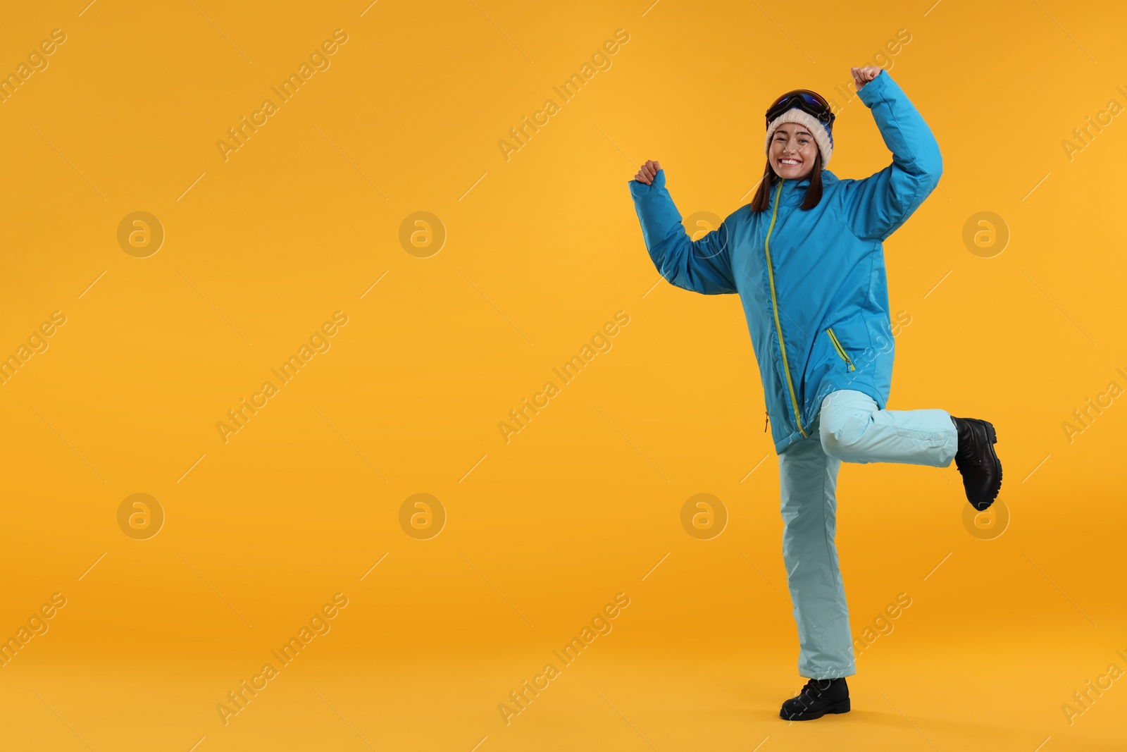 Photo of Winter sports. Happy woman with snowboard goggles on orange background, space for text
