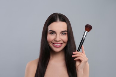 Happy woman with makeup brush on light grey background