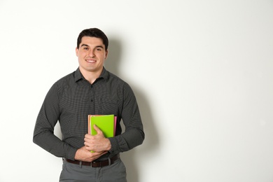 Portrait of male teacher with notebooks on light background