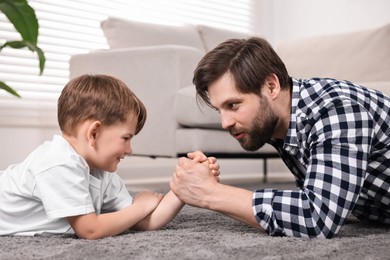 Photo of Arm wrestling. Dad playing with his son at home