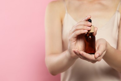 Photo of Young woman with bottle of essential oil on pink background, closeup. Space for text