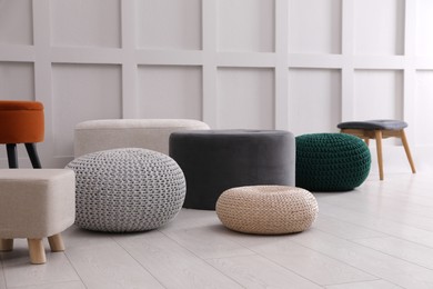 Different stylish poufs and ottomans near white wall