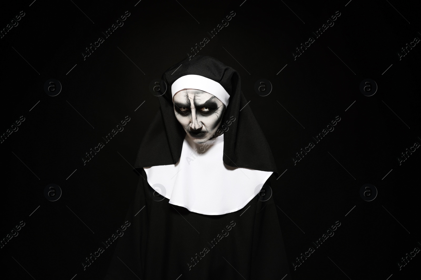 Photo of Portrait of scary devilish nun on black background. Halloween party look