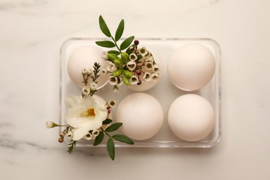 Photo of Easter eggs and beautiful flowers on white marble table, top view