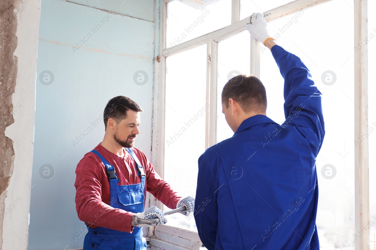 Photo of Workers dismantling old window with crowbar indoors