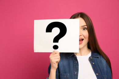 Emotional woman holding question mark sign on pink background