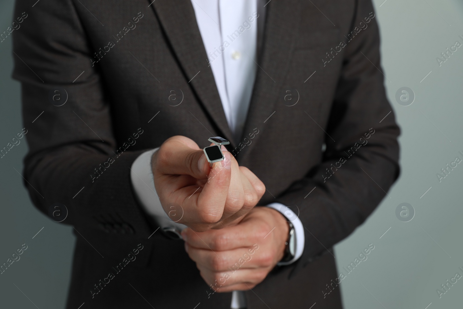 Photo of Stylish man holding cufflinks against grey background, closeup