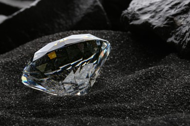 Beautiful shiny diamond on decorative black sand, closeup. Space for text