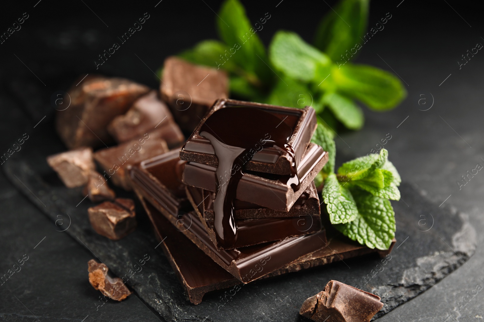 Photo of Tasty chocolate pieces with syrup and mint on black table, closeup