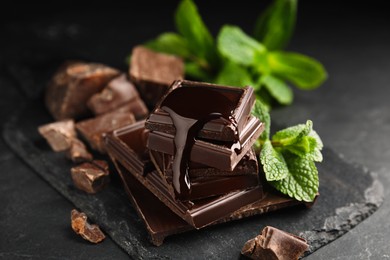 Tasty chocolate pieces with syrup and mint on black table, closeup