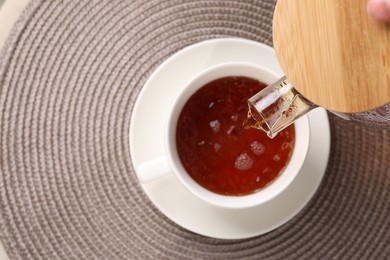 Photo of Pouring aromatic tea into cup at table, top view. Space for text