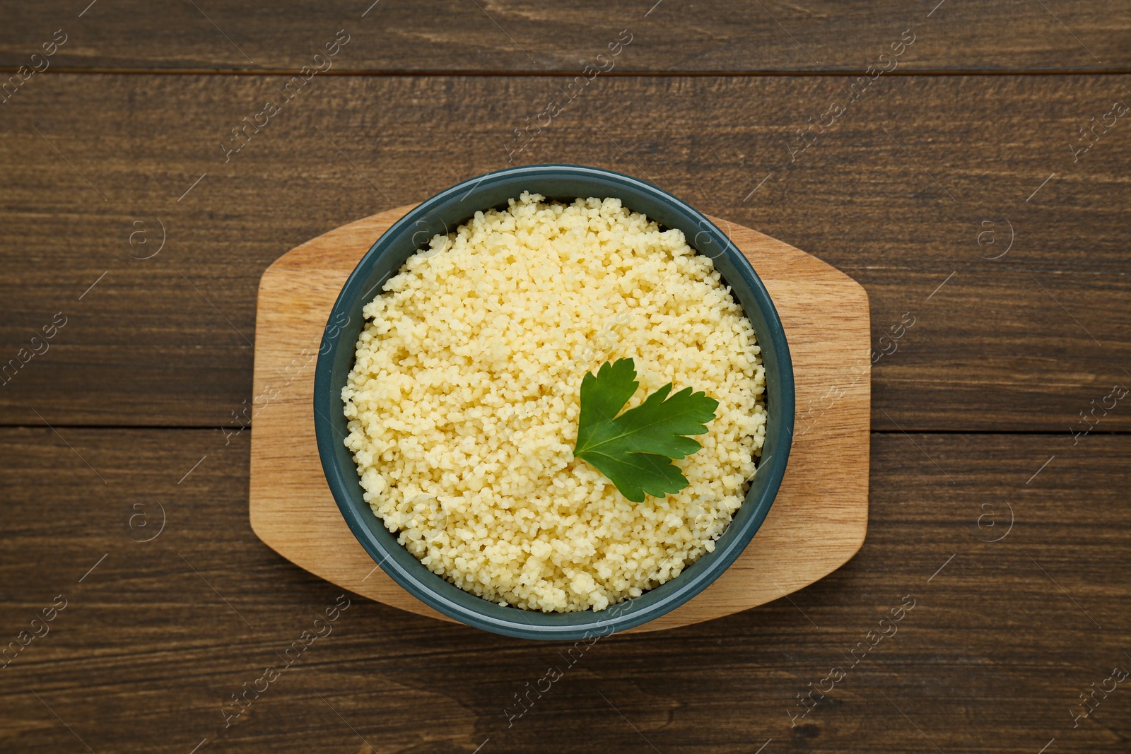 Photo of Tasty couscous with parsley on wooden table, top view