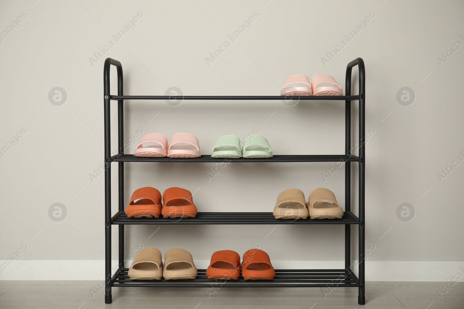 Photo of Shoe rack with different pairs of rubber slippers near white wall indoors