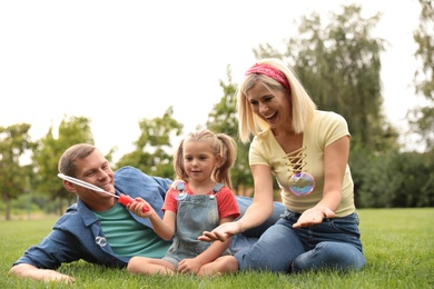 Photo of Happy family blowing soap bubbles in park on green grass