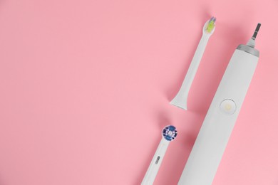 Photo of Electric toothbrush and replacement brush heads on pink background, flat lay. Space for text