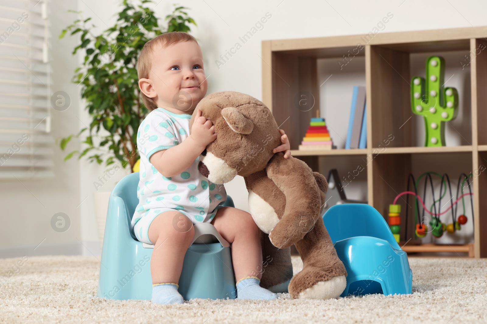 Photo of Little child and teddy bear sitting on plastic baby potties indoors