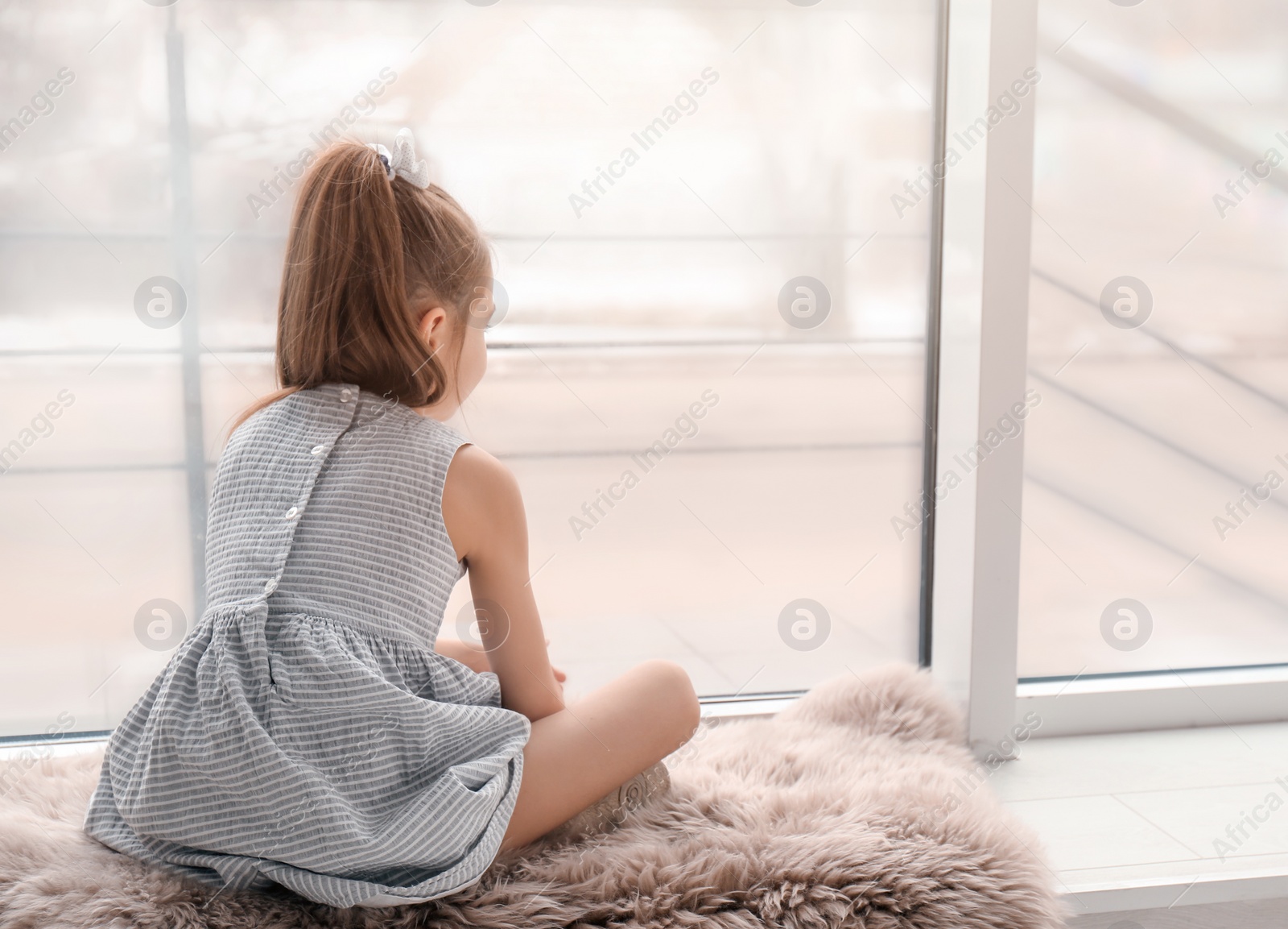 Photo of Lonely little girl sitting near window indoors. Child autism