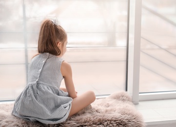 Lonely little girl sitting near window indoors. Child autism