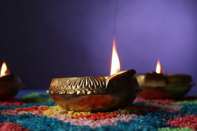 Photo of Diwali celebration. Diya lamps and colorful rangoli on table against violet background, closeup