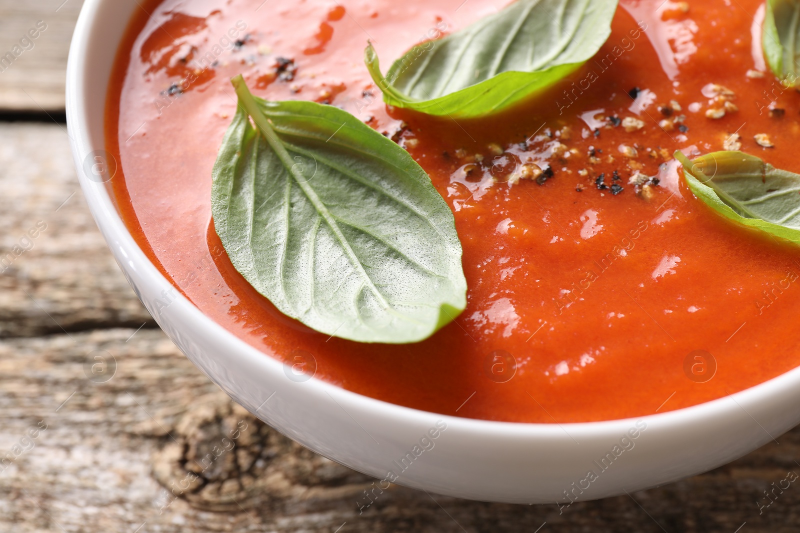 Photo of Delicious tomato soup with basil and spices on wooden table, closeup