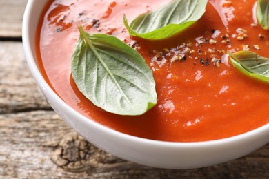 Photo of Delicious tomato soup with basil and spices on wooden table, closeup