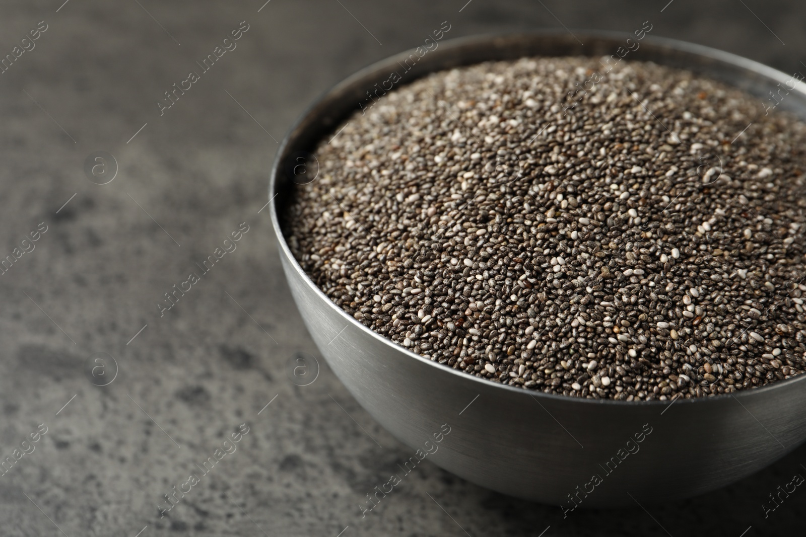 Photo of Metal bowl with chia seeds on grey table, closeup