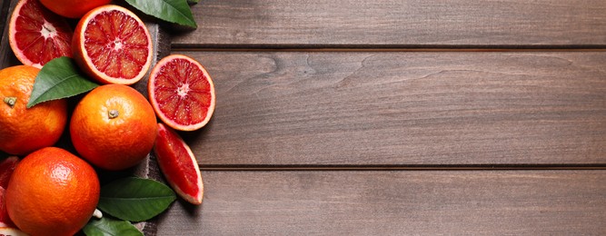 Ripe sicilian oranges with green leaves on wooden table, top view with space for text. Banner design