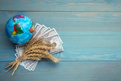 Photo of Globe, ears of wheat and banknotes on light blue wooden table, flat lay with space for text. Import and export concept