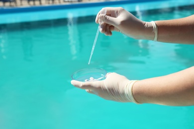 Photo of Woman dripping sample of swimming pool water into Petri dish to check PH level outdoors, closeup