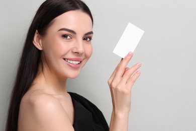 Photo of Happy woman holding blank business card on light grey background. Space for text