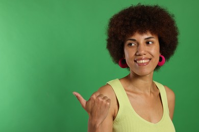 Photo of Happy young woman pointing at something on green background. Space for text