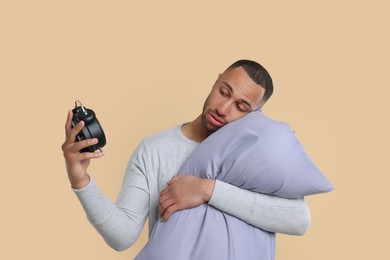 Photo of Sleepy man with pillow and alarm clock on beige background. Insomnia problem