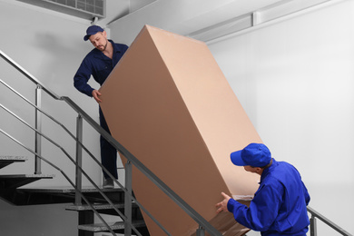 Photo of Professional workers carrying refrigerator on stairs indoors