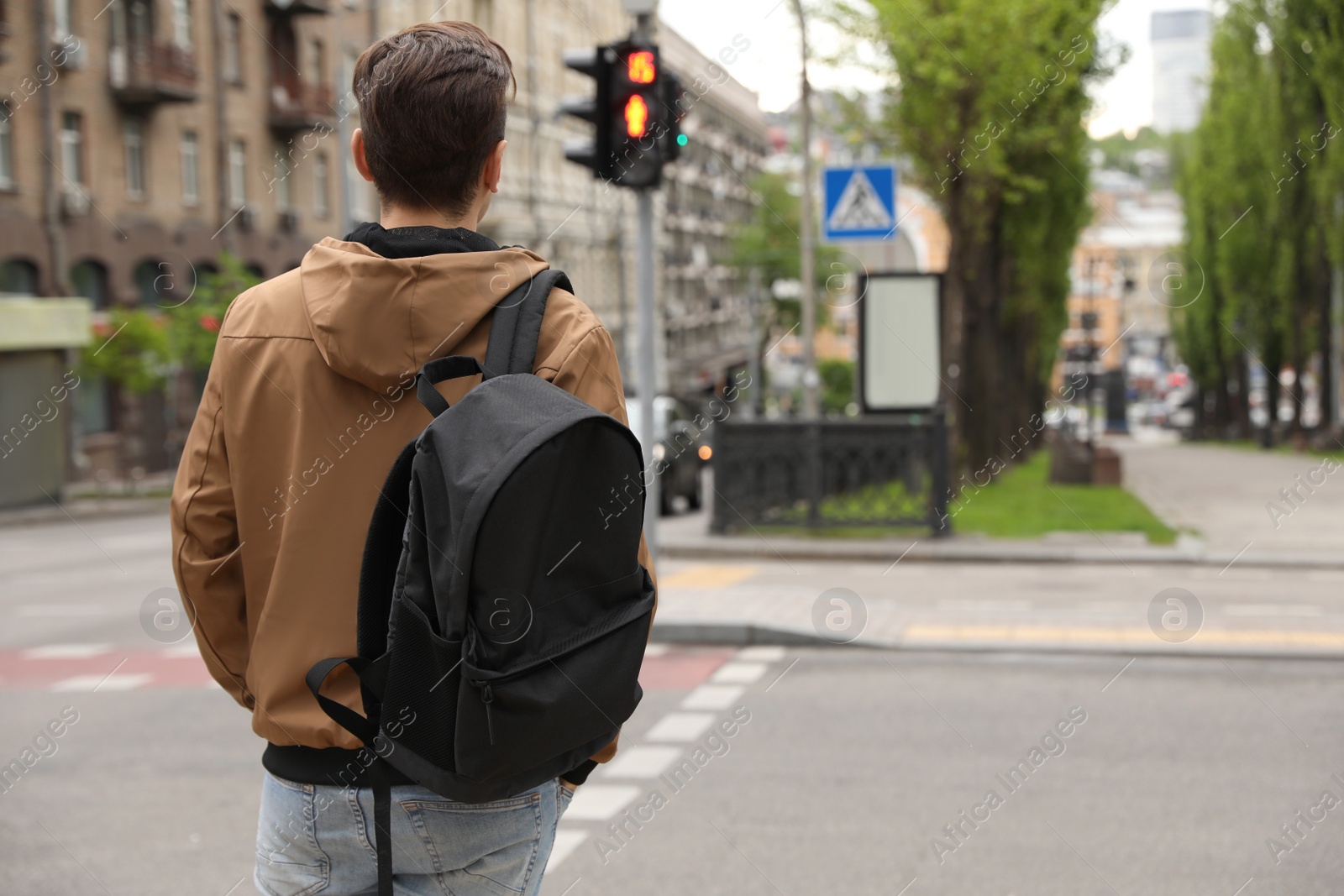 Photo of Young man waiting for traffic lights to cross street, back view