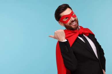 Photo of Businessman wearing red superhero cape and mask on light blue background. Space for text
